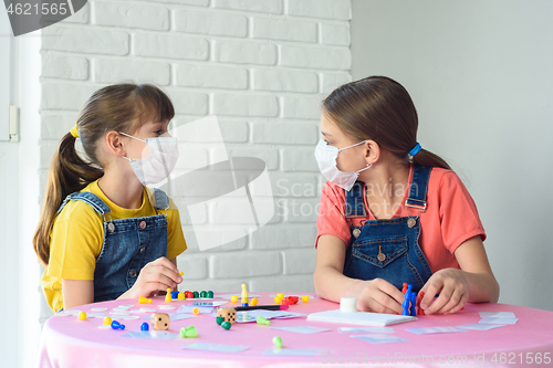 Image of Two girls in protective medical masks in quarantine play board games