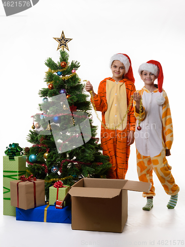 Image of Two girls stand by the Christmas tree and hold festive tinsel in their hands.