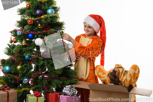 Image of One girl hangs a ball on the Christmas tree, the other climbed into the box with her head