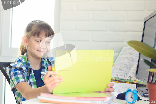 Image of A girl sits at a table and happily looks at the screen of a tablet computer