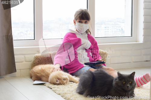 Image of A sick quarantined girl sits on the floor with a tablet, cats are lying next to the carpet