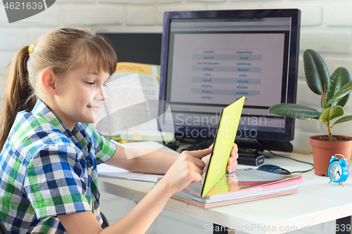 Image of A girl is studying at home, watching a remote lesson on a tablet