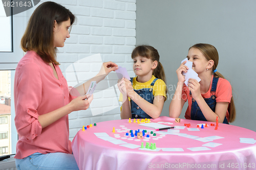 Image of In the process of a board game, mom chooses a card from her daughter\'s hand