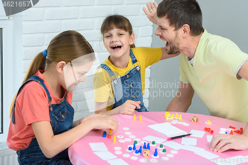 Image of The girl and dad are screaming and laughing cheerfully, the other girl is considering the next move in the board game