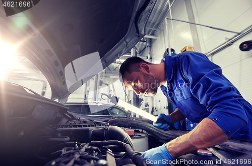 Image of mechanic man with lamp repairing car at workshop