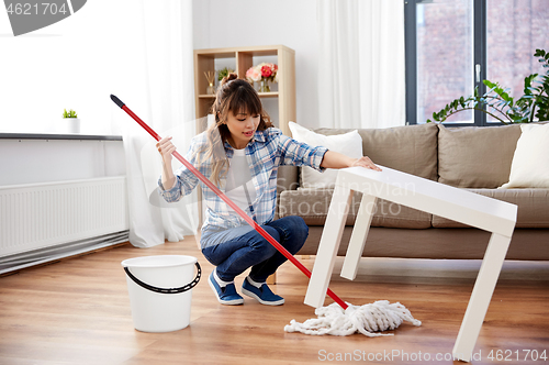 Image of happy asian woman with mop cleaning floor at home