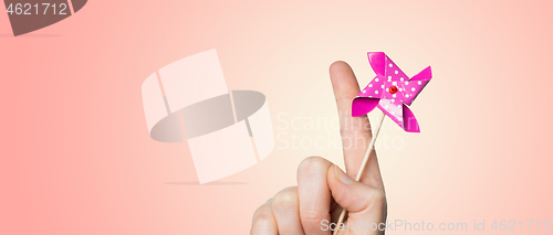 Image of close up of hand holding pinwheel toy over pink