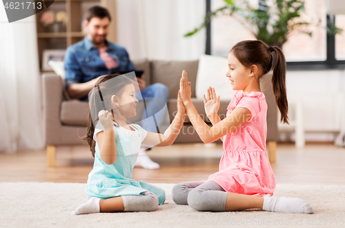 Image of happy little sisters playing clapping game at home