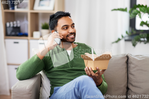 Image of smiling indian man eating takeaway food at home