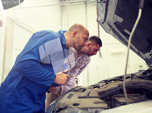 Image of auto mechanic with clipboard and man at car shop