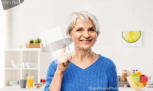 Image of smiling senior woman pointing finger up in kitchen