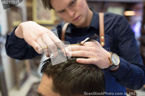 Image of male hairdresser cutting hair at barbershop