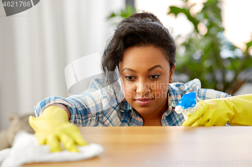 Image of african american woman cleaning table at home