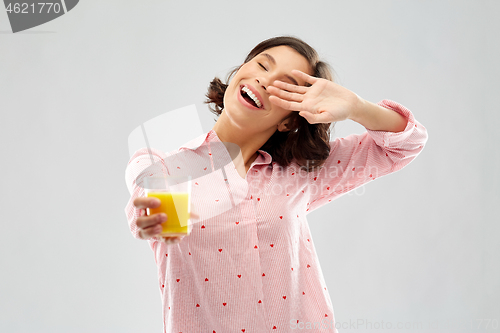 Image of happy yawning young woman in pajama with juice