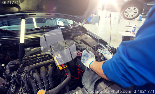 Image of auto mechanic man with multimeter testing battery