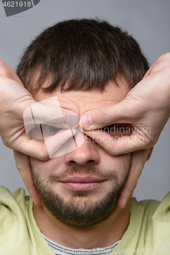 Image of Close-up portrait of a man who made with his hands a kind of glasses on the eyes of European appearance