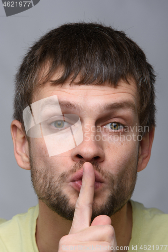 Image of Portrait of a man of European appearance who put a finger to his mouth, gesture of silence, close-up