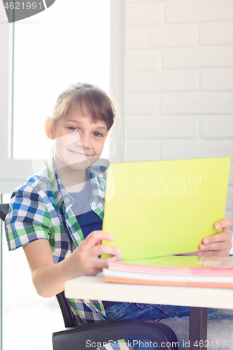 Image of A girl with a tablet sits at a table at home and joyfully looked into the frame