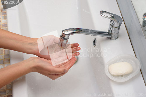 Image of Girl pours water in the palm of the hand in the bathroom