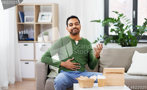 Image of pleased indian man eating takeaway food at home