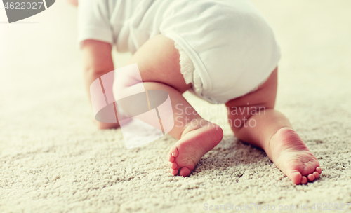 Image of little baby in diaper crawling on floor at home