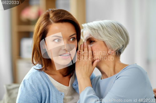 Image of senior mother whispering to adult daughter at home