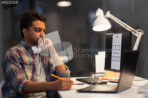 Image of creative man with laptop working at night office