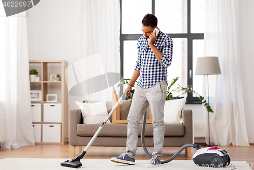 Image of man with vacuum cleaner calling on cell at home