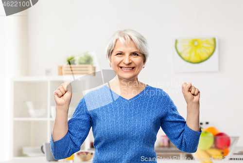 Image of happy senior woman celebrating success in kitchen