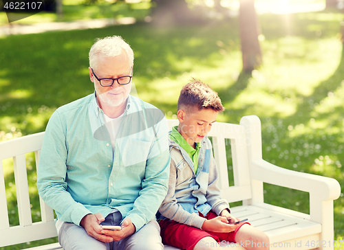 Image of old man and boy with smartphones at summer park