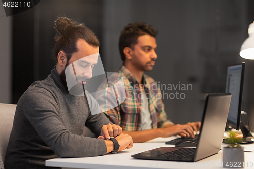 Image of creative man with smartwatch works at night office