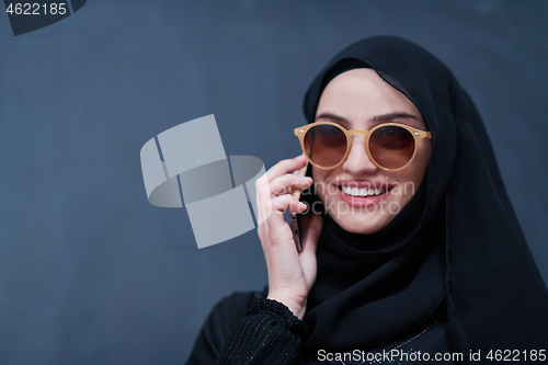 Image of young muslim woman wearing sunglasses using smartphone