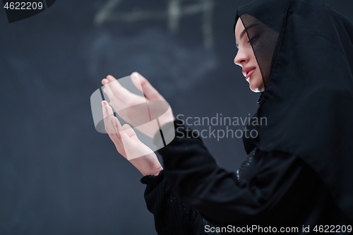 Image of muslim woman making traditional prayer to God in front of black 