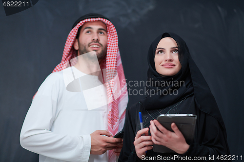 Image of muslim couple using modern technology in front of black chalkboa