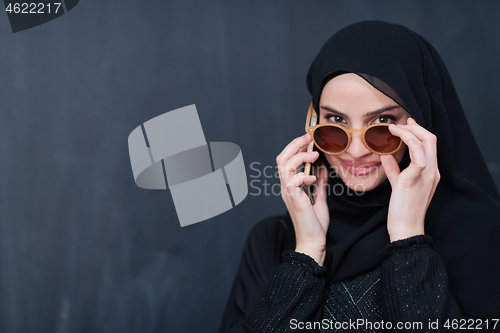 Image of young muslim woman wearing sunglasses using smartphone