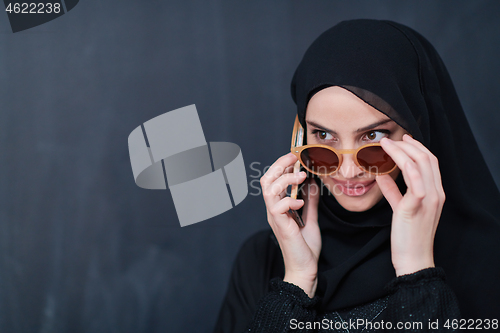 Image of young muslim woman wearing sunglasses using smartphone