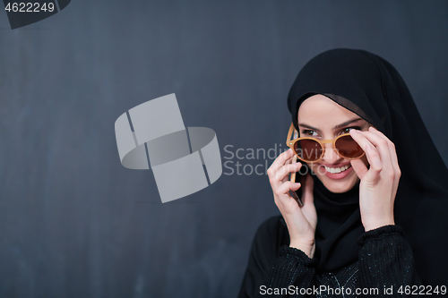 Image of young muslim woman wearing sunglasses using smartphone