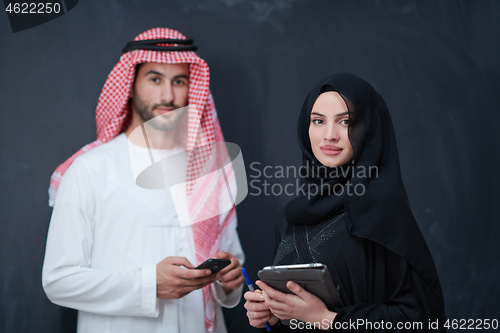 Image of muslim couple using modern technology in front of black chalkboa