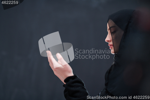 Image of muslim woman making traditional prayer to God in front of black 