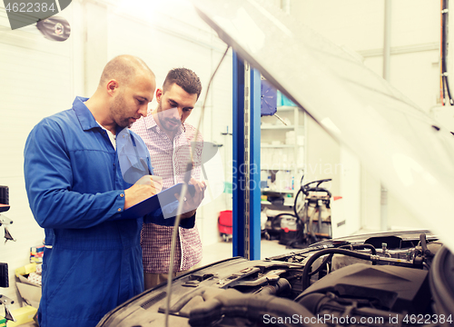 Image of auto mechanic with clipboard and man at car shop