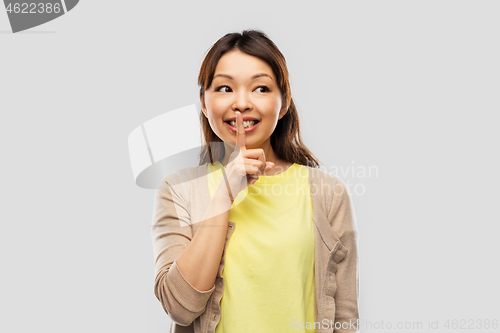 Image of happy asian woman with finger on lips