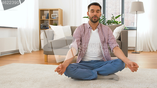 Image of man with tablet computer meditating at home