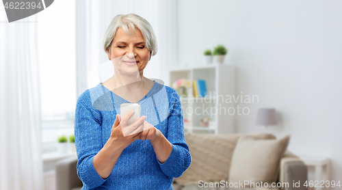 Image of smiling senior woman using smartphone at home