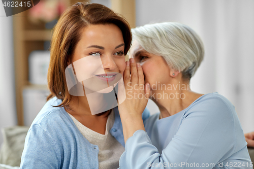 Image of senior mother whispering to adult daughter at home