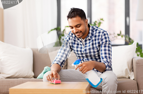 Image of indian man cleaning table with detergent at home