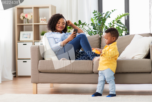 Image of mother using smartphone and baby playing toy car