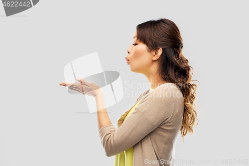 Image of asian woman holding something on hand and blowing