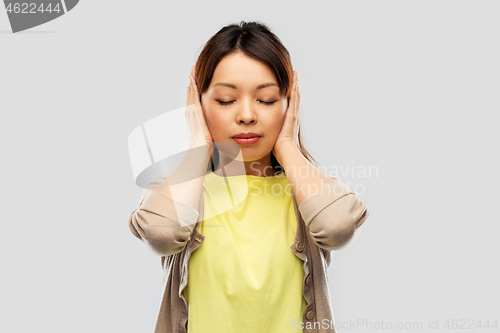 Image of asian woman closing ears by hands