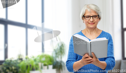 Image of senior woman in glasses reading book at home