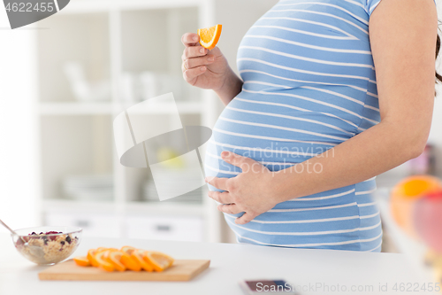 Image of close up of pregnant woman eating orange at home